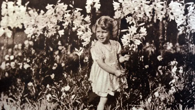 Princess Elizabeth later Queen Elizabeth II, as a child, gathering flowers in a garden.