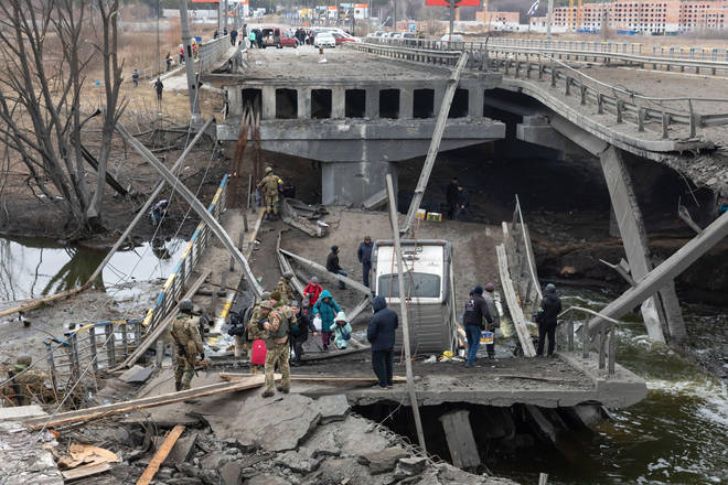 People cross a destroyed bridge as they evacuate the city of Irpin