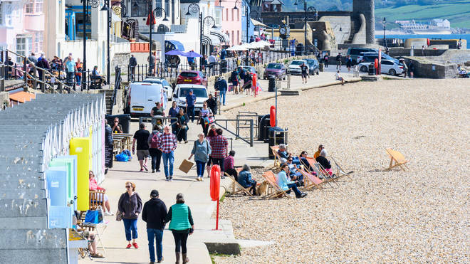 People sit in the sun and walk along the shorefront on a beach in Dorset.