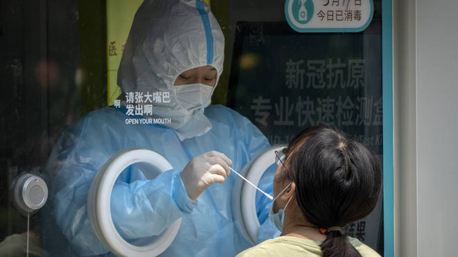 A worker wearing a protective suit administers a Covid-19 test at a coronavirus testing site in Beijing
