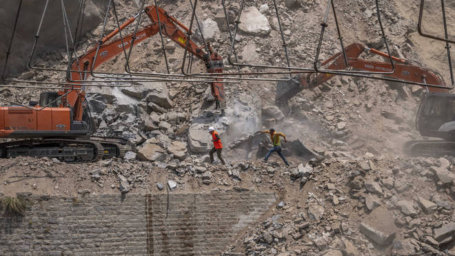 Rescue workers run for cover as earth movers dig through rubble of a collapsed tunnel in Ramban district, south of Srinagar, Indian controlled Kashmir, on Friday May 20 2022