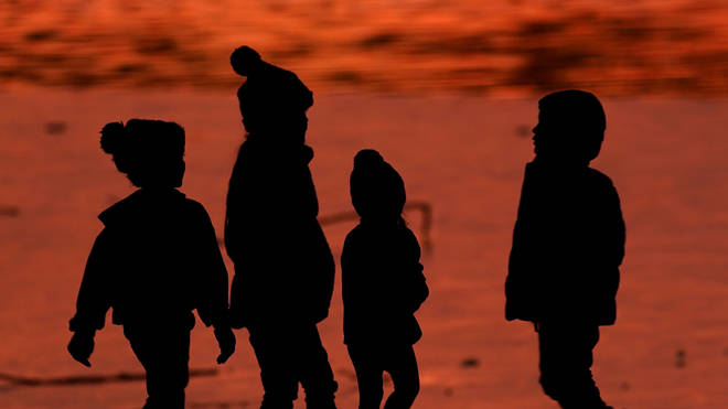 Children are silhouetted against a pond at a park