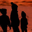 Children are silhouetted against a pond at a park