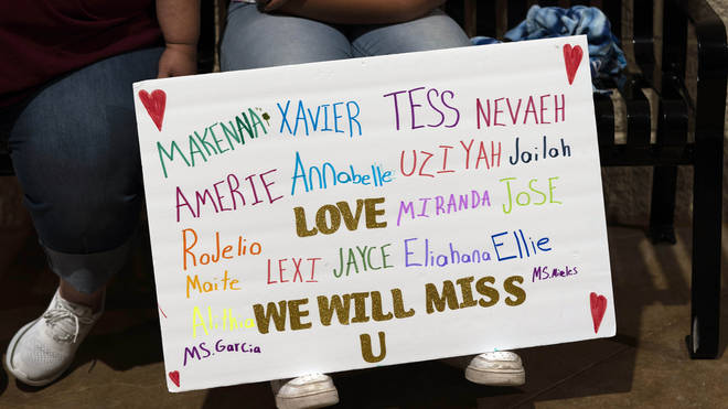 Stormy Flores, 11, sits with a sign bearing the names of the Robb Elementary School shooting victims