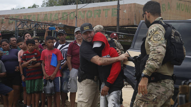 A federal police officer escorts a suspect towards a river in the area where Indigenous expert Bruno Pereira and freelance British journalist Dom Phillips disappeared