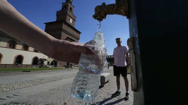 Tourists fill plastic bottles with water from a public fountain at the Sforzesco Castle in Milan, Italy
