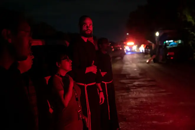 Local priests from the San Antonio Archdiocese stand near the scene where a tractor-trailer was discovered with migrants inside