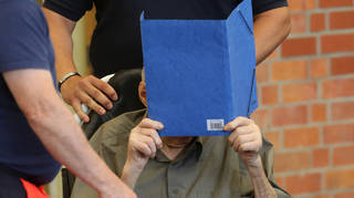 Former Nazi concentration camp guard covers his face as he arrives at a gym used as a makeshift courtroom
