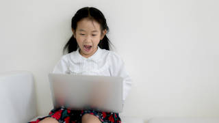 A girl reacts in shock while using a laptop