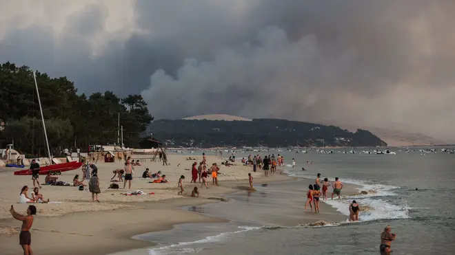 People swim on a beach as smoke rises from a forest fire in La Teste-de-Buch in Gironde