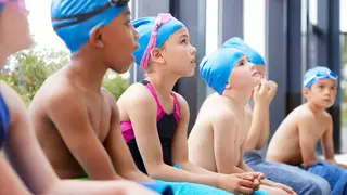 Children sit by a pool waiting for a lesson but LBC can reveal nearly half of children in Wales can't swim