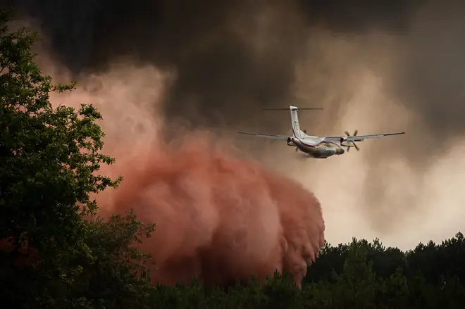 A firefighting aircraft sprays fire retardant over trees during a wildfire near Saint-Magne