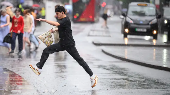 A man leaps over a puddle as shoppers rush through a heavy downpour