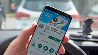 A driver holds a phone showing the Waze app