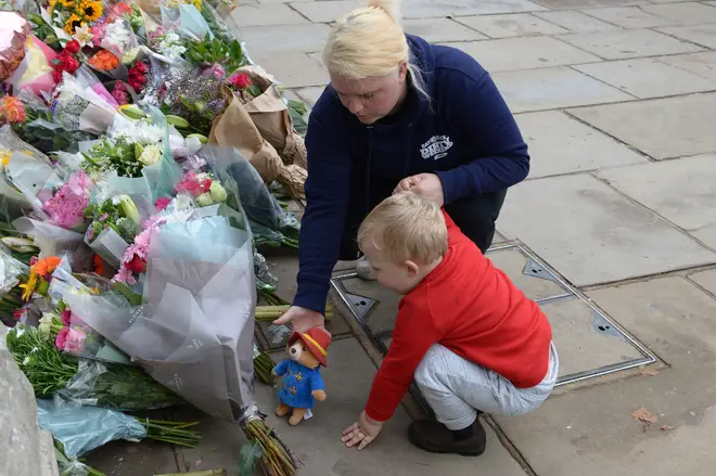 A young boy leaves a toy Paddington Bear and flowers for the Queen