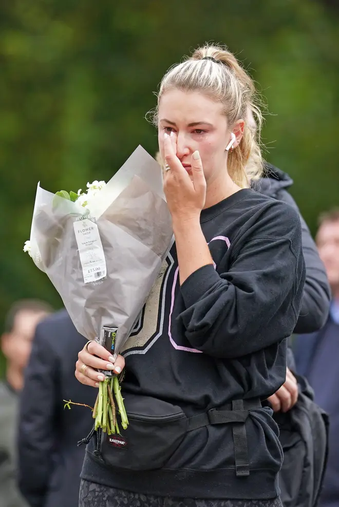 A woman wipes away a tear as she stands with a bouquet of flowers outside Buckingham Palace