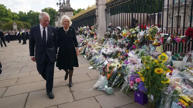 King Charles and Camilla, the Queen Consort, walk past floral tributes at the gates of Buckingham Palace
