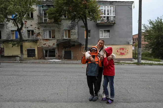A woman posing with her children in front of a destroyed building in Izyum, Kharkiv Region