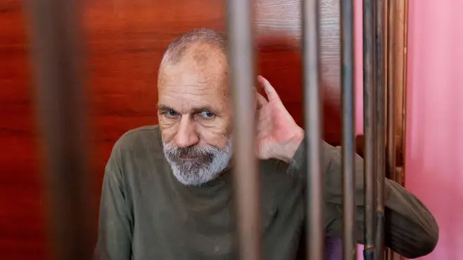John Harding, aged in his 50s, sits inside a defendants' cage during a court hearing in Donetsk, Ukraine