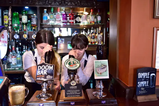 Two bartenders pulling pints behind hand beer pumps in Tap & Spile Birmingham pub, UK