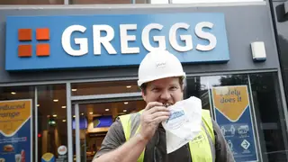 A workman eats a snack outside a Greggs store