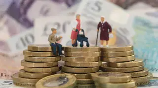 Models of elderly people on a pile of coins and banknotes