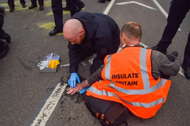 A police officer dissolves the superglue on the hand of an Insulate Britain activist blocking the traffic in Parliament Square yesterday