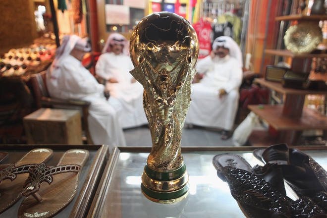 Arab men sit at a shoemaker's stall with a replica of the World Cup trophy