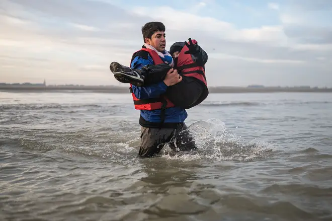 A migrant carries a child as he runs to board a smuggler's boat on the beach of Gravelines, near Dunkirk, northern France on October 12, 2022