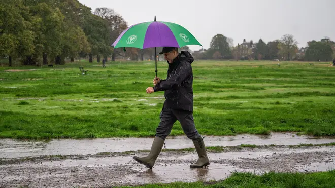 A pedestrian with an umbrella walks on a waterlogged Wimbledon Common this morning.