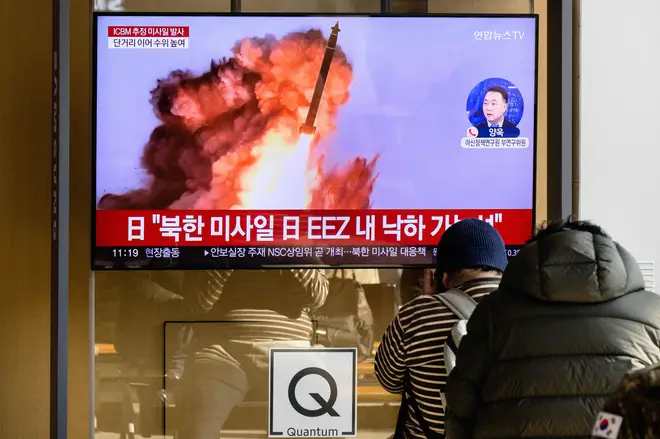 People sit near a television showing a news broadcast with file footage of a North Korean missile test, at a railway station in Seoul