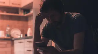 Depressed man typing text message on mobile phone in dark room, selective focus