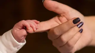 A baby's hand holding an adult's finger