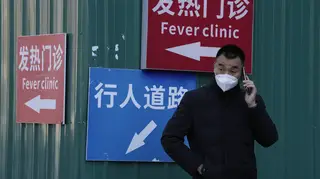 A man wearing a mask talks on his phone near a sign for a fever clinic in Beijing