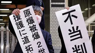 Noboru Sakiyama, left, head of the plaintiffs, holds a banner outside Nagasaki District Court