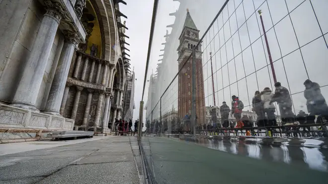 Tourists and residents use walkways to cross a flooded St Mark's Square in Venice