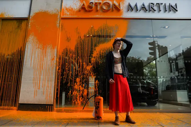 A member of the environmental activist group Just Stop Oil reacts after spraying orange paint on the window shop of the Aston Martin car show room, in central London