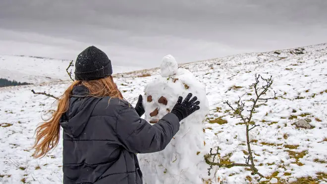 A young woman builds a snowman amid freezing weekend temperatures in Wales