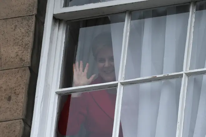 Nicola Sturgeon waves from a window, after holding a press conference, as people gather outside of Bute House