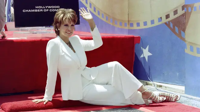 Actress Raquel Welch waves to photographers and fans as she sits in front of her newly unveiled star on the Hollywood Walk of Fame