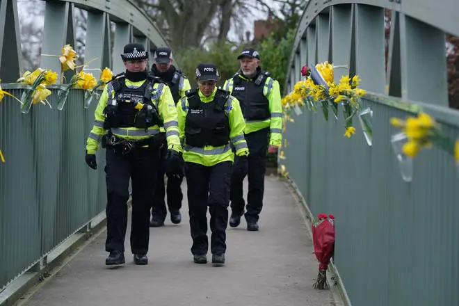 Police officers walk past flowers and yellow ribbons tied to a bridge over the River Wyre in St Michael's on Wyre.