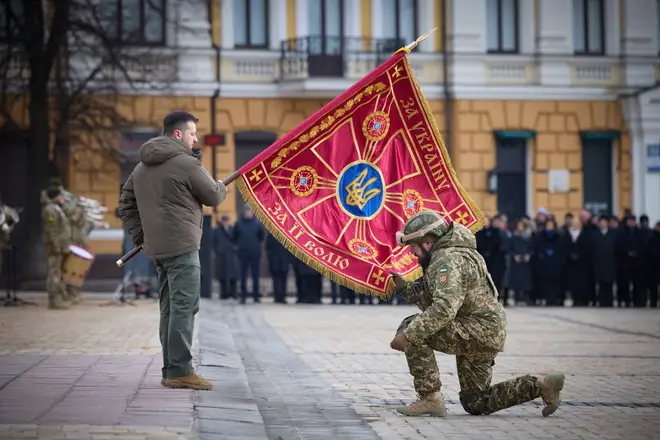 Ukrainian President Volodymyr Zelenskyy, left, holds the flag of a military unit as an officer kisses it, during commemorative event on the occasion of the Russia Ukraine war
