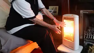 A woman warming herself with an electric fire