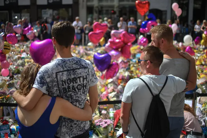 Couples comfort one another as flowers and balloons are left in Saint Ann's Square in tribute to those killed in an explosion at the Manchester Aren