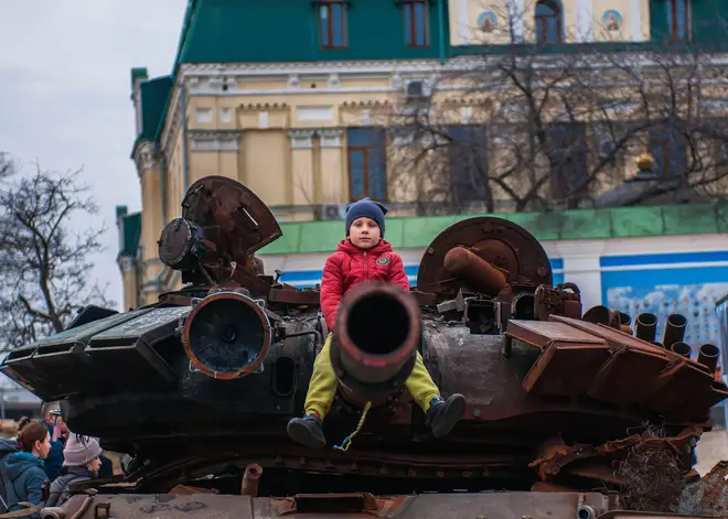 A child sits on the canon of a tank destroyed by Ukrainian armed forces in Kyiv