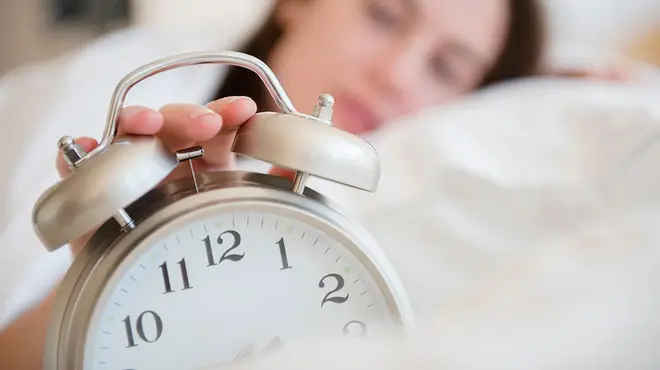 Woman turning off her alarm clock from bed