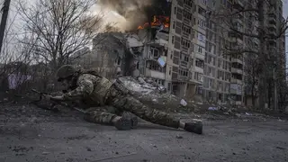 A Ukrainian police officer takes cover in front of a burning building hit in a Russian airstrike in Avdiivka