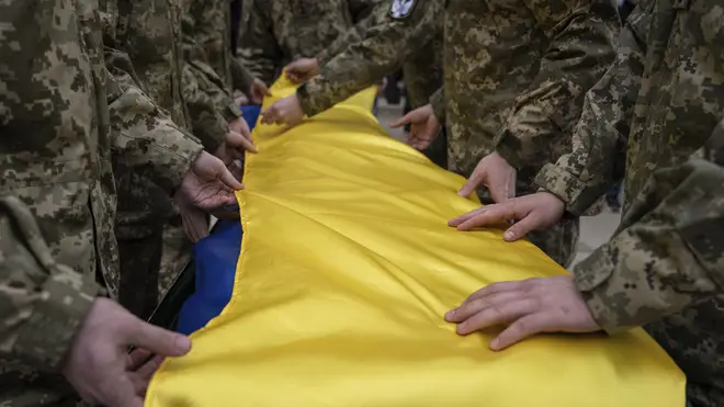 Ukrainian servicemen fold the national flag over the coffin of a comrade during a funeral