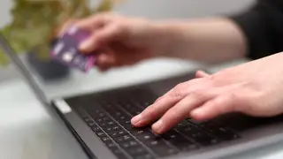 Someone using a laptop and holding a bank card