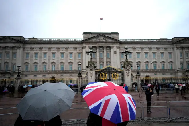 Buckingham Palace in the rain as tourists walk past with a union jack umbrella